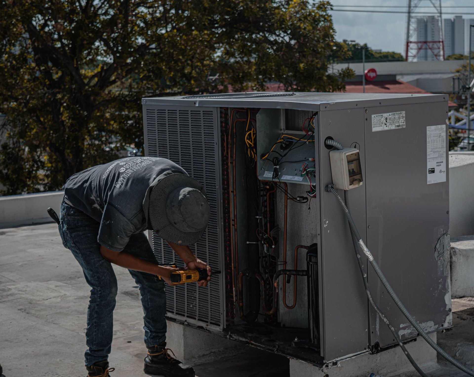 A technician is repairing an air conditioning unit on a rooftop, demonstrating skilled manual work.